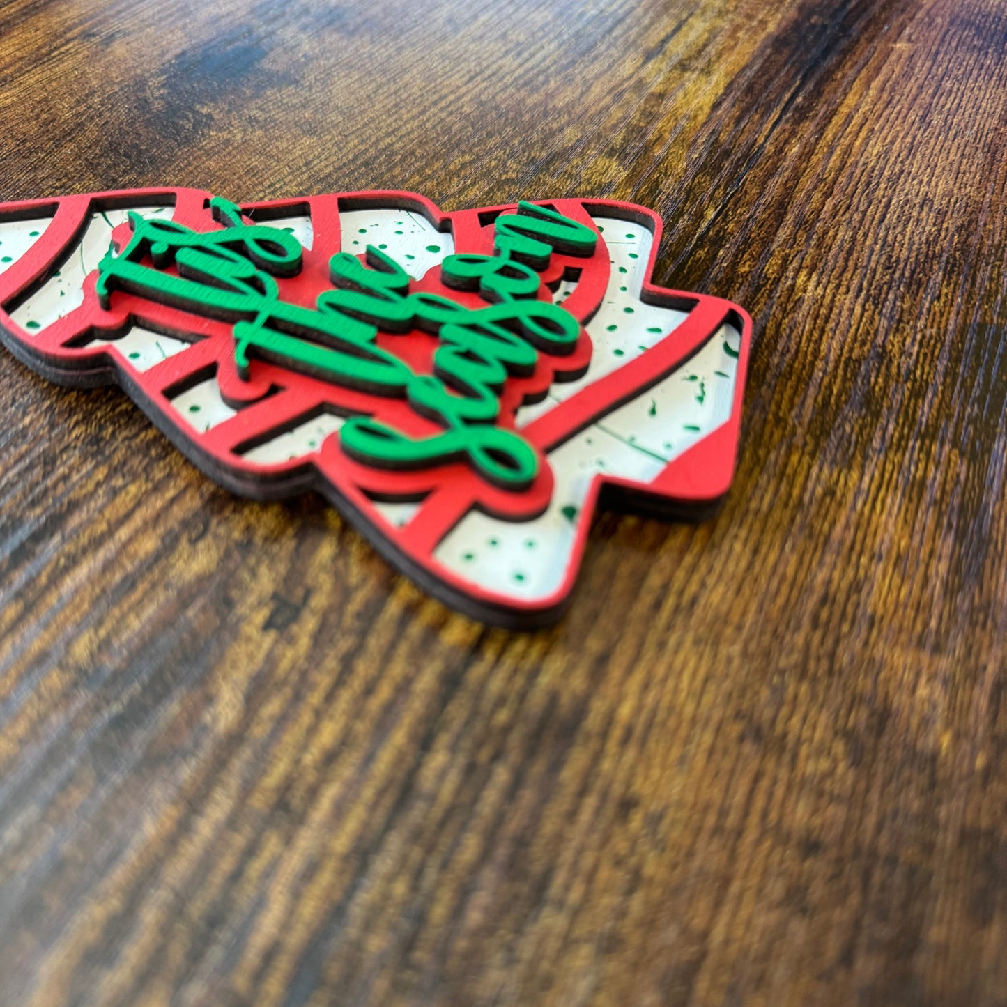Decorative Christmas tree ornament with 'Tis the Season' text on a wooden surface