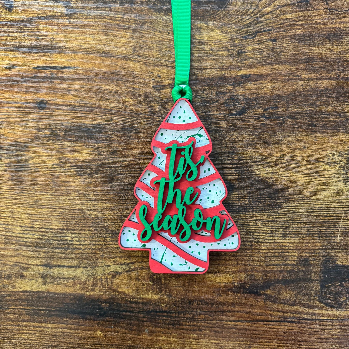Decorative Christmas tree ornament with 'Tis the Season' text on a wooden surface
