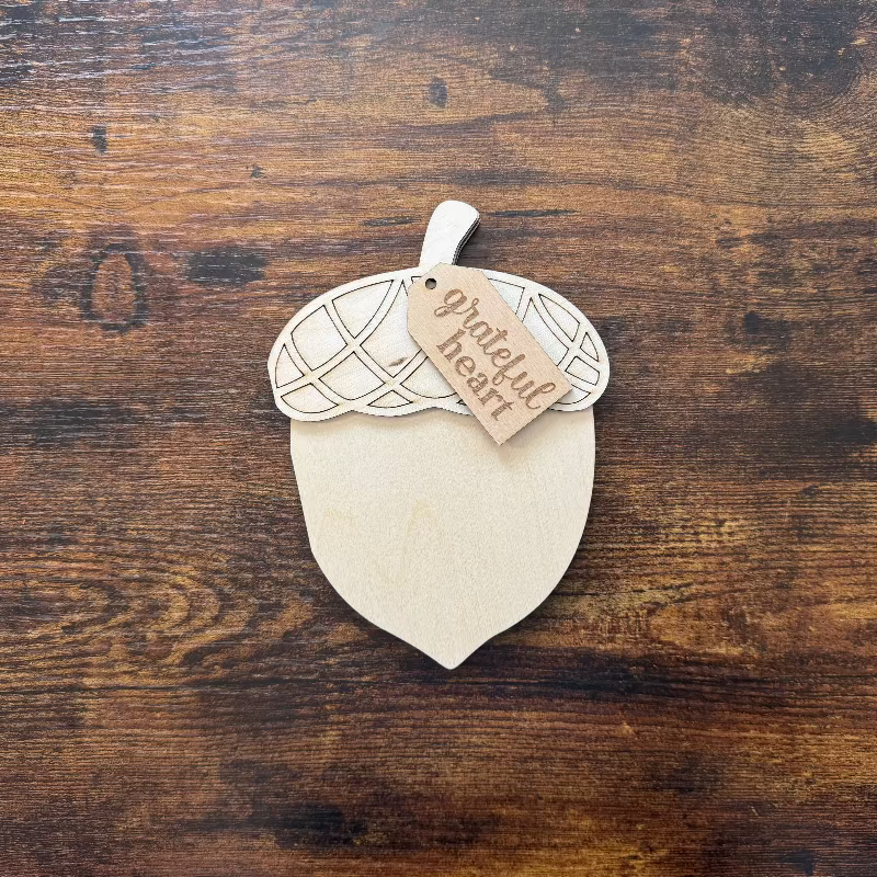 Wooden acorn-shaped shelf sitter with a 'grateful heart' tag on a wooden surface