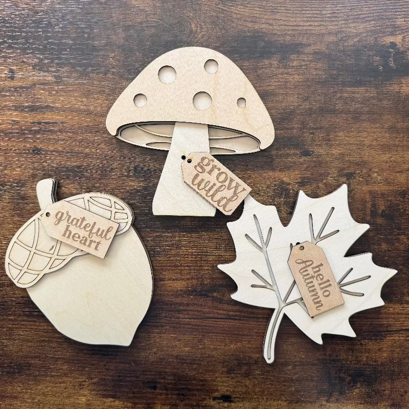 Wooden decorations shaped like a mushroom, acorn, and leaf on a wooden surface