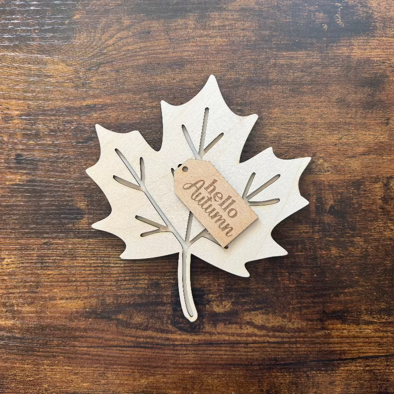 Wooden leaf-shaped decoration with 'hello Autumn' tag on a wooden surface
