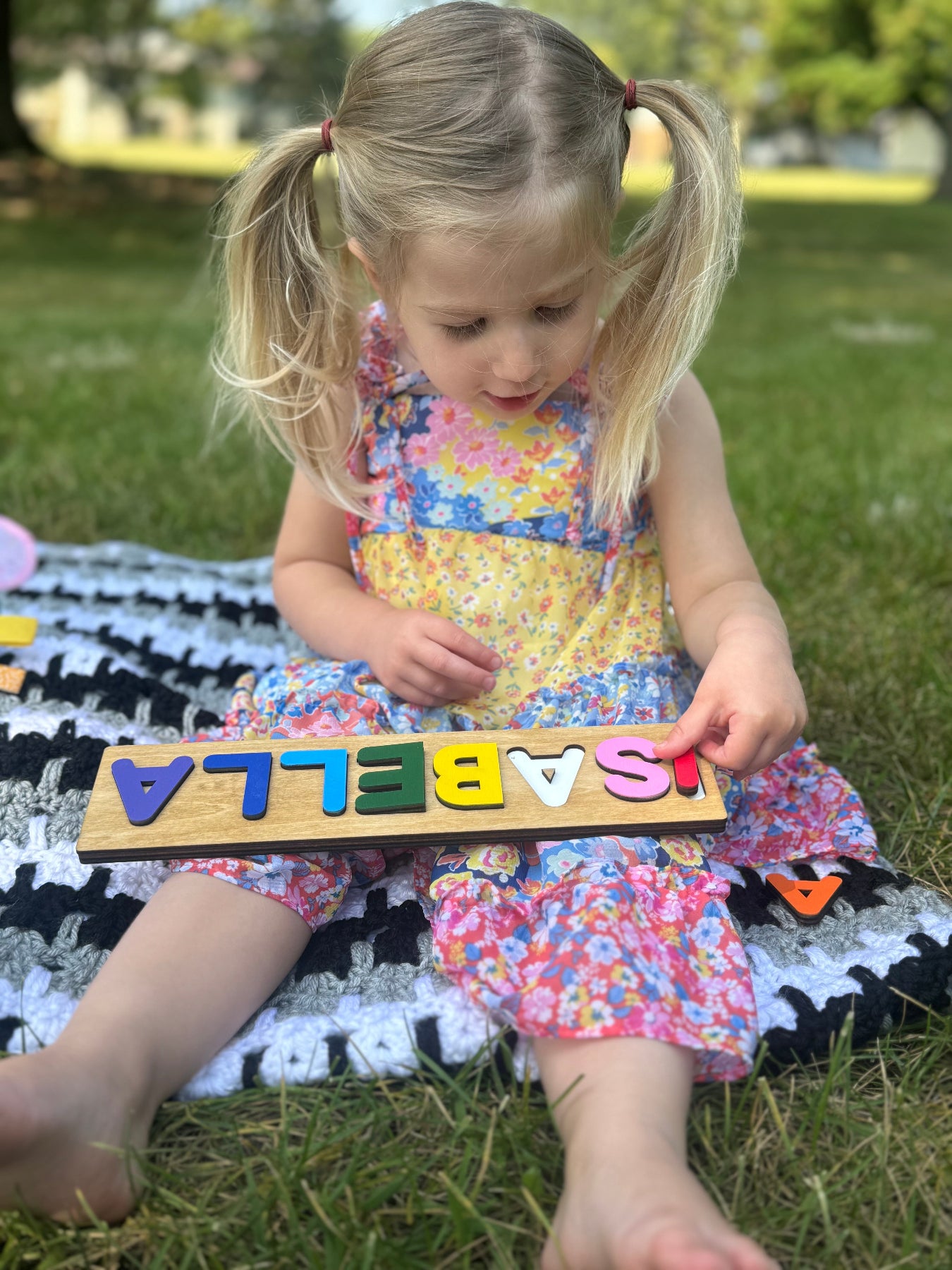 Child playing with a wooden alphabet puzzle outdoors on a grassy area.