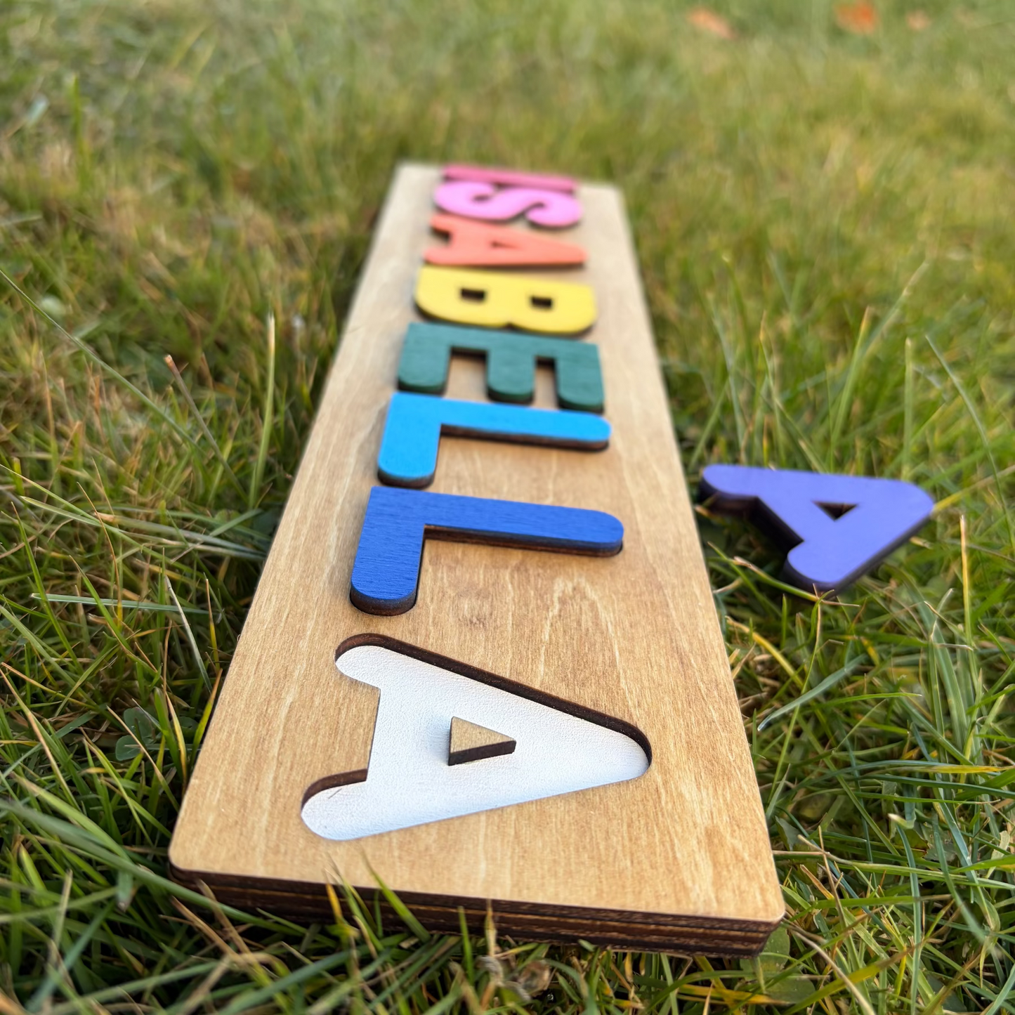 Wooden name puzzle with colorful letters on a grassy background