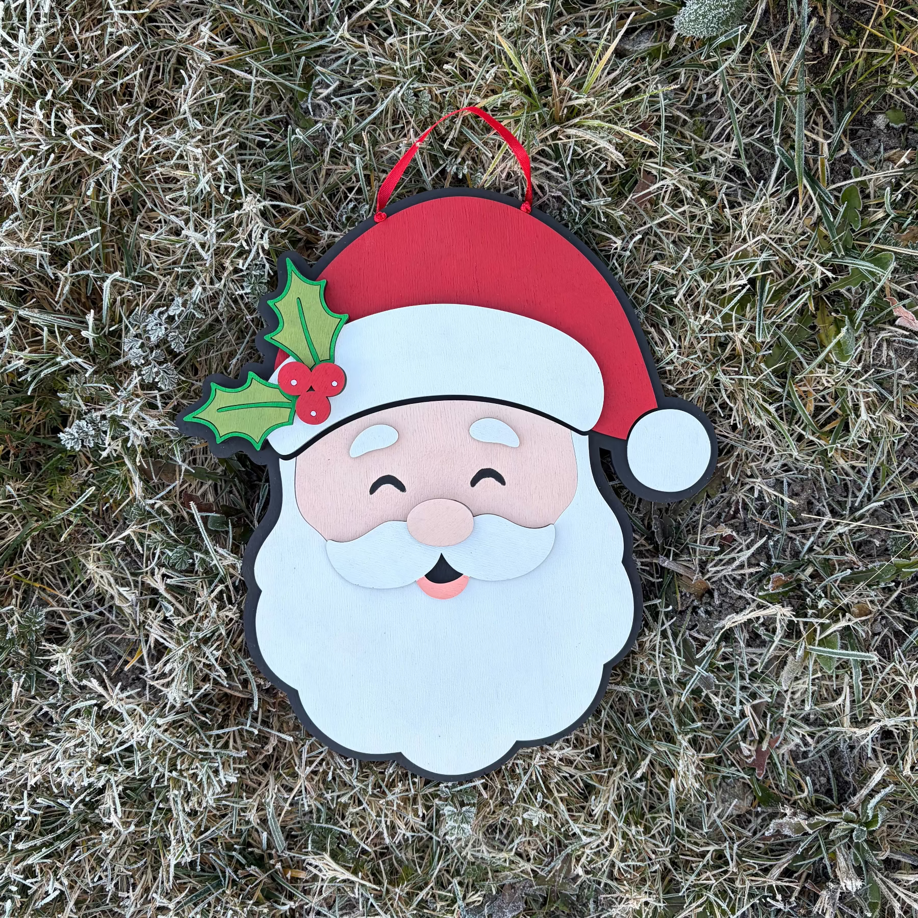 Decorative 3D Wood Santa Claus door hanger with a red hat and holly leaf on a frosty bush background
