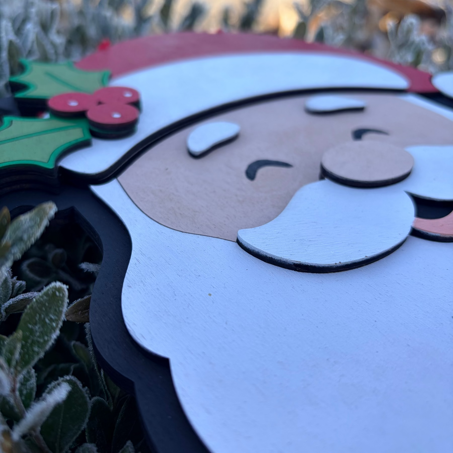 Close-up of a decorative Christmas Santa shaped door sign, wearing a red hat with holly leaves and berries.